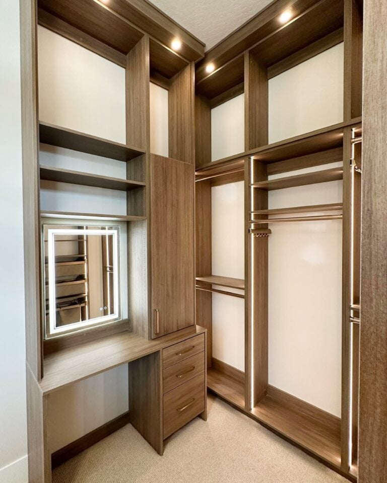 Walk-in closet with dark wood cabinetry, open shelves, drawers, and a built-in vanity with a framed mirror lighting.