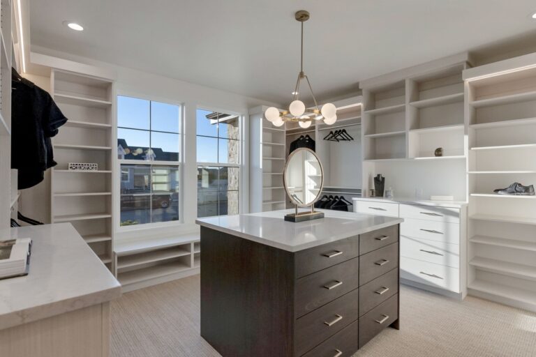 Bright walk-in closet with white built-in shelves, a dark wood island with a marble top, and a round mirror under a modern chandelier.