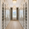 Long, bright walk-in closet with white built-in wardrobes, glass doors, and gold handles along both walls; light wood floor and ceiling lights.