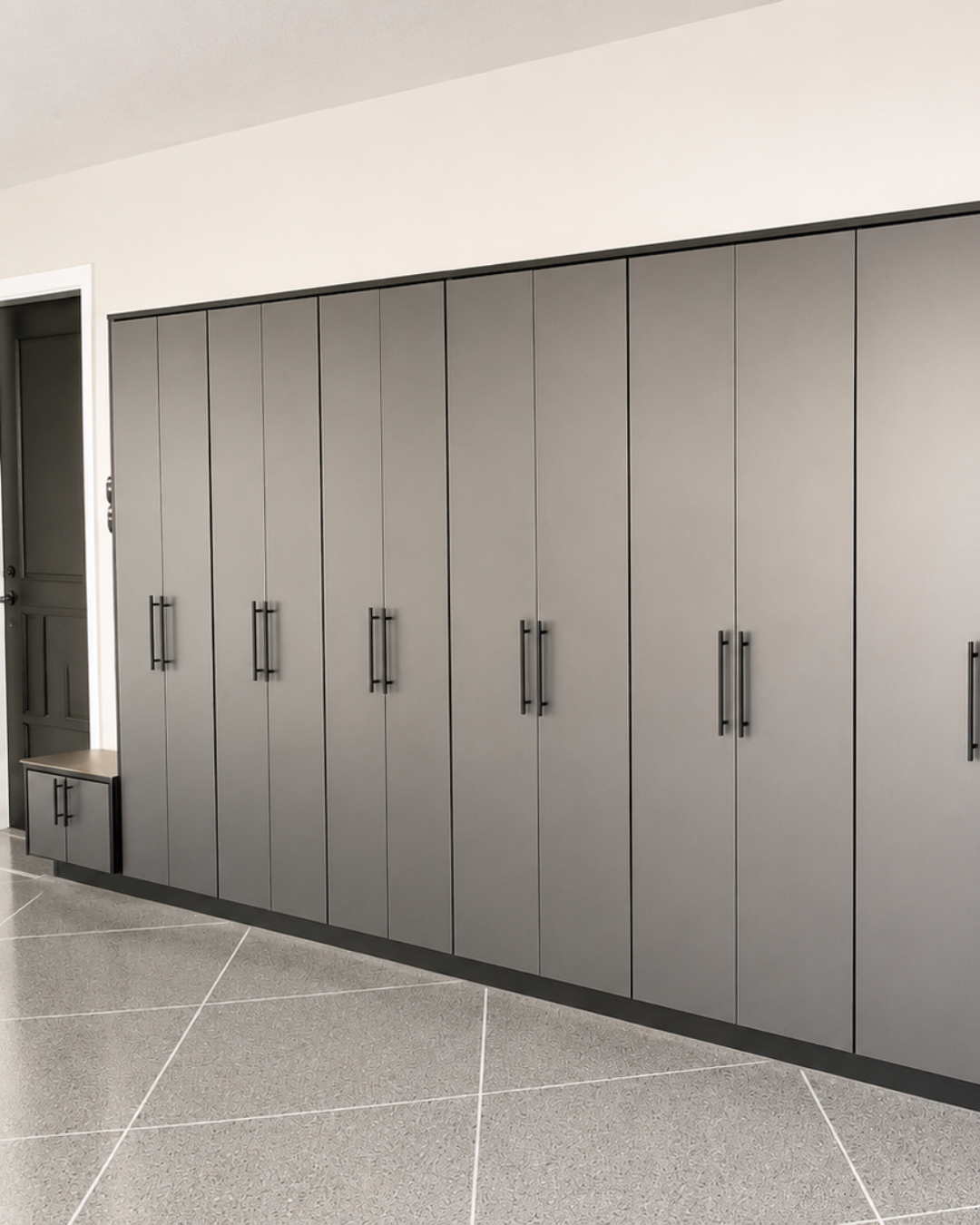 tall gray storage cabinets Row of tall gray storage cabinets with black handles along a wall, next to a small bench by a door on the left.
