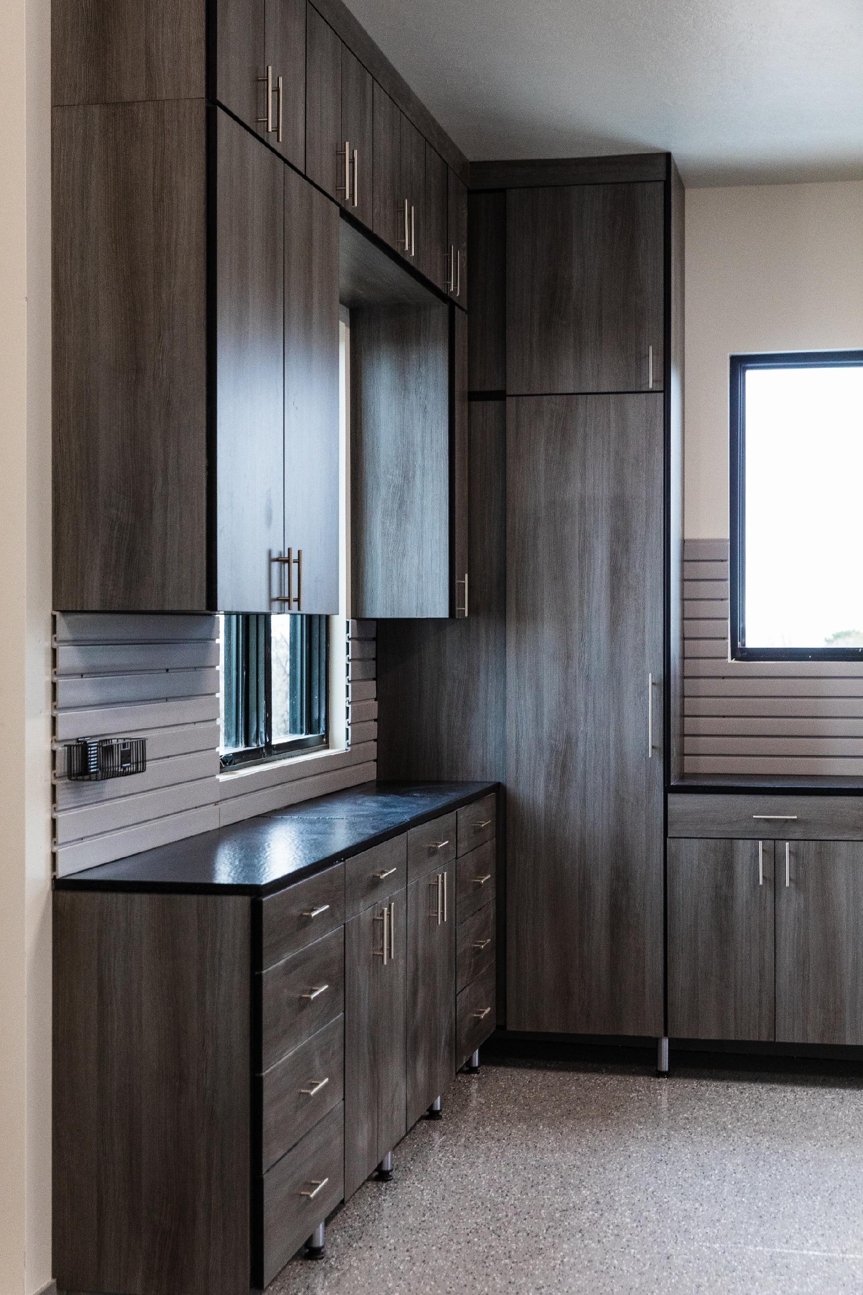 dark wood cabinets and drawers for garage Garage with dark wood cabinets and drawers along two walls, stainless handles, and a granite countertop. A window with white blinds is on the right.