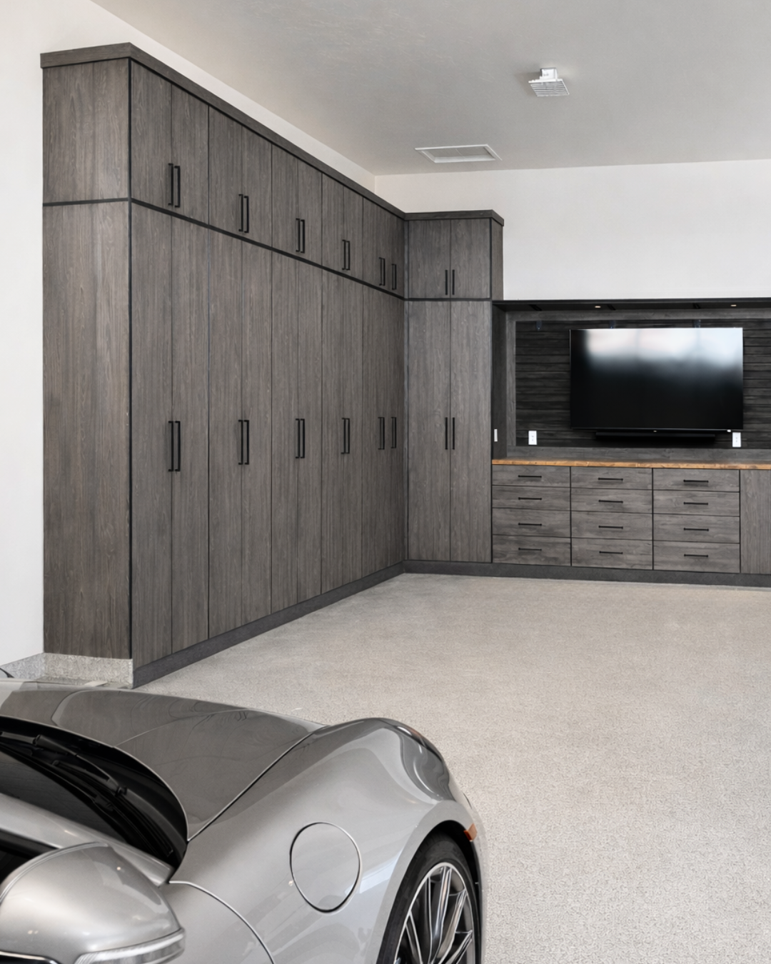 Modern garage with tall dark wood cabinets along the left wall and a silver sports car in the foreground.