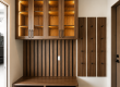 Wood-toned entryway with upper cabinets and glass-front doors, a slatted wall behind a bench, and vertical coat-hook panels beside the door.