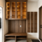 Wood-toned entryway with upper cabinets and glass-front doors, a slatted wall behind a bench, and vertical coat-hook panels beside the door.