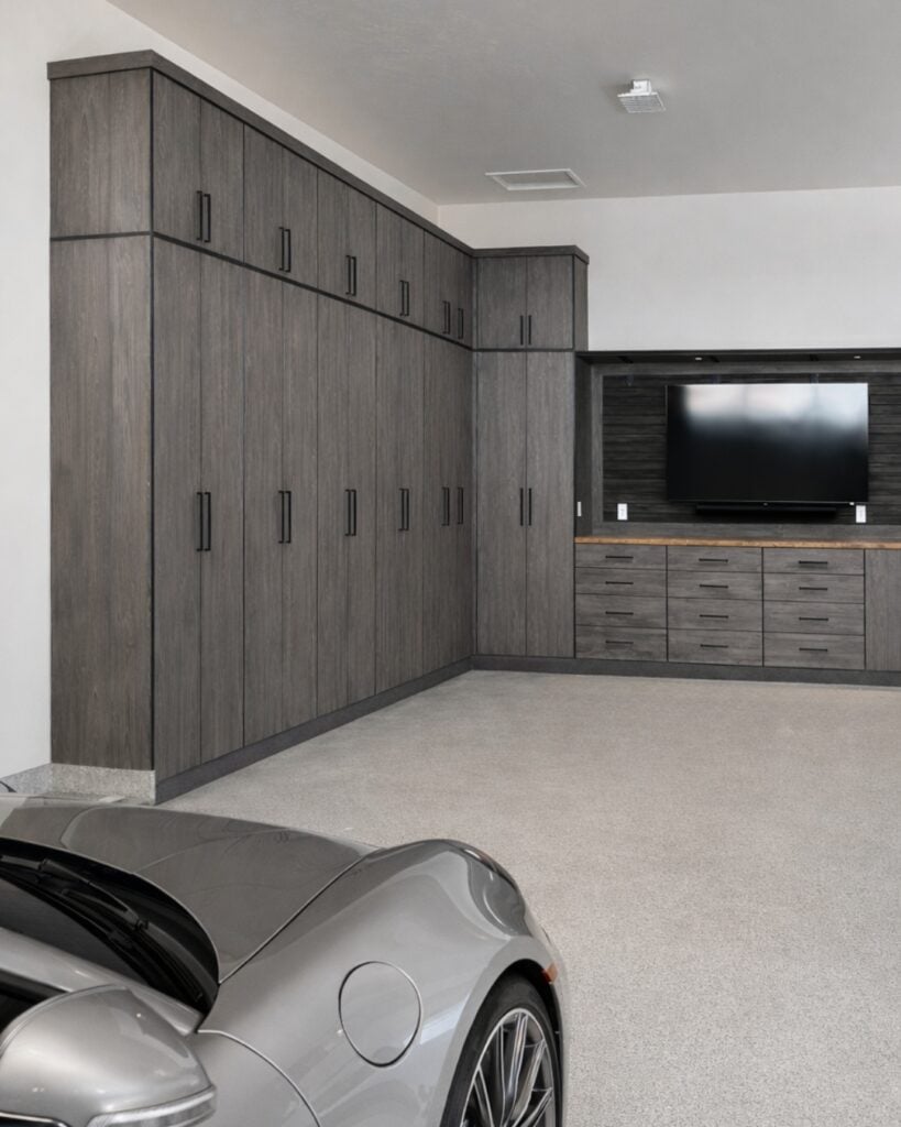 Garage interior with tall gray wood cabinets along the wall and a built-in storage counter with drawers; a silver sports car parked in the foreground.