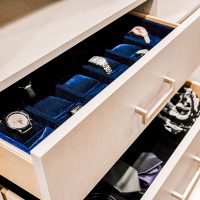Custom closet drawer featuring luxurious blue lining, neatly organized with an array of watches, jewelry, and ties, showcasing exquisite craftsmanship.